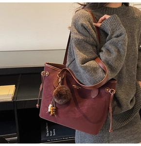 Detail of burgundy tote bag with gold hardware and plush pom-pom charm on a model