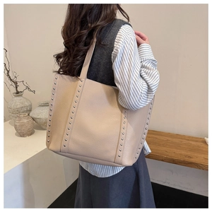 Close-up of beige tote bag with silver rivet details and lychee grain leather texture