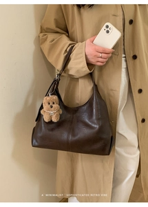 Detail of dark brown leather tote bag featuring a cute plush bear pendant and retro texture