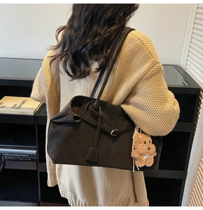 Detail of dark brown suede tote bag featuring a leather buckle strap and plush bear charm