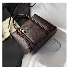 Detailed view of dark brown litchi grain leather handbag with beaded tassel and strap