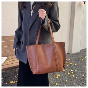 Close-up of brown pebbled leather tote bag with silver rivets and autumn vibes