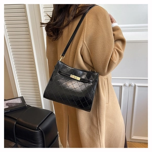 Detail view of the black quilted shoulder bag with gold clasp worn over a camel wool coat