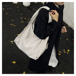 Detail of a large cream canvas hobo bag with wide shoulder strap on a black coat