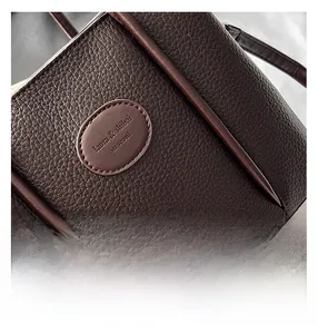 Close-up of brown lychee grain leather bucket bag with wooden bead tassel and logo detail