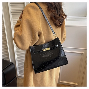 Detail of a black quilted leather shoulder bag with a gold metal turn-lock on a model