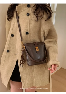 Detail of dark brown matte leather bucket bag with gold clasp and ring on a wool coat