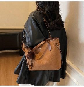 Detail of vintage brown tote bag featuring decorative plush charm and wooden bead tassel