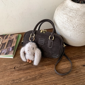 Detail of vintage Boston bag in dark coffee suede with a plush rabbit charm on wood