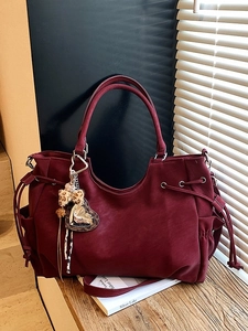 Deep red large tote bag with side drawstrings and leopard charm on wooden stairs