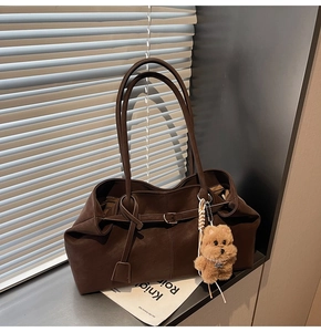 Detail of dark brown suede tote bag featuring metallic buckle and plush puppy charm