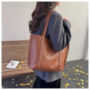 Detail of silver rivets and lychee grain leather texture on brown tote bag side view