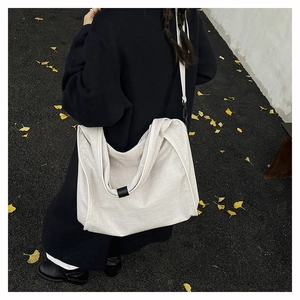 Detail view of a large cream canvas crossbody bag worn over a black autumn coat