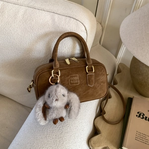 Detail of dark brown suede Boston bag with gold hardware and a grey plush bunny charm