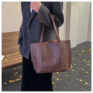 Detail of dark brown lychee leather tote bag with silver metal rivets and dual straps