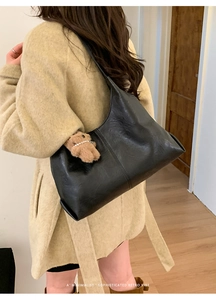Close-up of black retro leather tote bag featuring a cute teddy bear charm and pearl chain