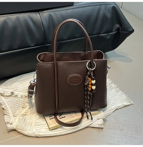 Close-up of dark brown lychee grain leather tote bag with stylish beaded pendant detail