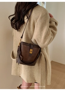 Detail of a dark brown retro leather bucket bag with a gold buckle worn as a crossbody
