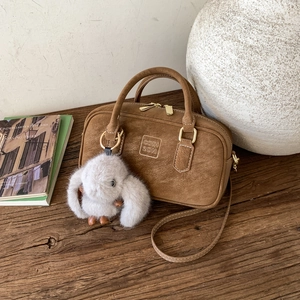 Brown suede bowling bag detail featuring a plush rabbit pendant and embossed brand logo