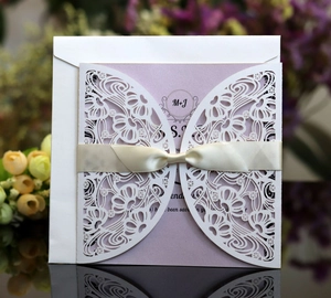Close-up of laser-cut wedding invitation with glitter insert and beige silk ribbon bow