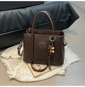 Detail of dark brown lychee leather bucket bag with wooden bead tassel and shoulder strap