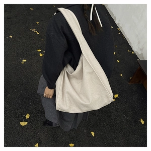 Close-up of beige woven fabric hobo bag on dark asphalt ground with autumn leaves