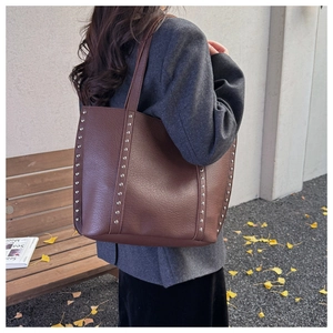 Close-up of brown pebbled leather tote bag with silver rivets carried by a model