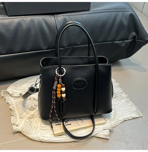 Detail of black pebbled leather bucket bag with top handles and beaded charm accessory