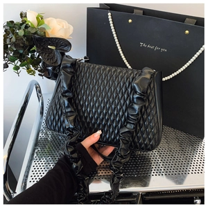 Detail of black quilted shoulder bag with ruffles and glossy leather texture