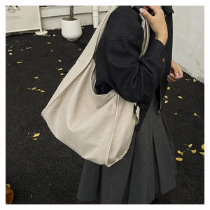 Fashionable oversized beige canvas hobo bag for women worn as a shoulder bag in street style