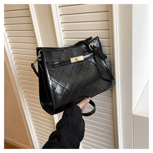 Close-up of black quilted glossy shoulder bag with golden metallic rectangular lock