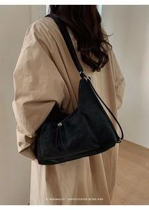 Detailed side view of a large black vintage tote bag worn over a beige winter coat
