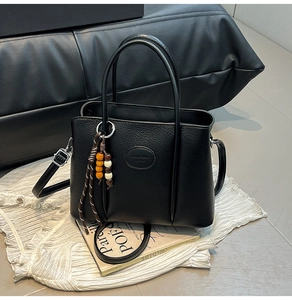 Detail of black litchi grain leather bucket bag with decorative beaded charm and strap