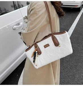 Detail einer weißen Plüschtasche mit braunen Lederriemen und Perlenanhänger