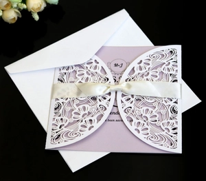 Detail of laser-cut floral wedding invitation with purple insert and silk ribbon bow