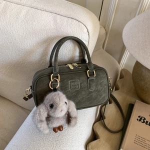 Detail of olive Boston bag with textured leather and a plush rabbit charm on a sofa