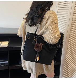 Détail d'un sac cabas en cuir noir avec un pompon en peluche et un logo doré élégant