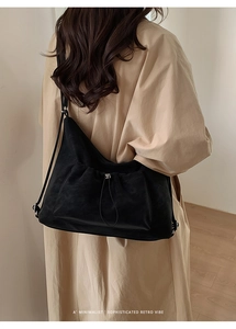Black minimalist shoulder bag with drawstring detail styled on a trench coat