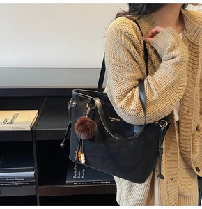 Détail du sac cabas en daim noir avec logo doré et porte-clés pompon en fourrure marron