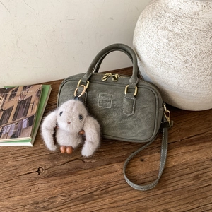 Detail of dark green textured leather handbag with plush rabbit charm and embossed logo