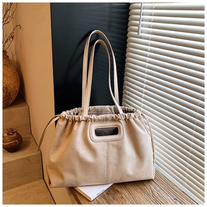 Détail du sac cabas en daim beige avec fermeture à cordon sur une surface en bois
