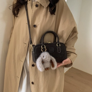 Close-up of retro brown suede pillow bag with embossed logo and rabbit plush pendant