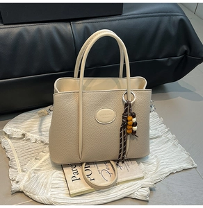 Detail of beige lychee leather bucket bag with logo patch and beaded charm