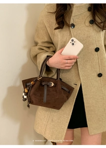 Close-up of brown suede tote bag with golden buckle and decorative beaded handle detail