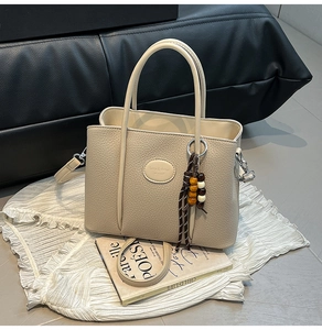 Close-up of beige bucket bag in lychee leather with wooden bead charm and top handles