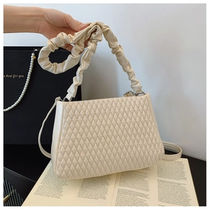 Detail of beige quilted shoulder bag featuring a unique gathered ruched strap design