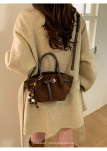 Détail d'un sac cabas en daim marron foncé avec perles sur un manteau en laine beige