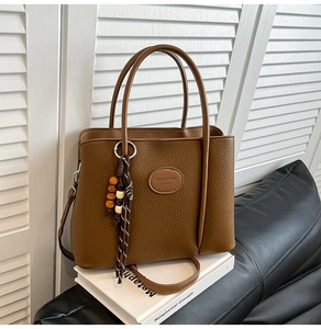 Detail of brown litchi leather bucket bag with beaded charm and brand logo tag