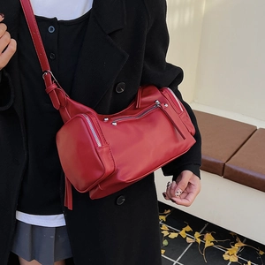 Chic red cylindrical crossbody bag with silver hardware on a black coat background