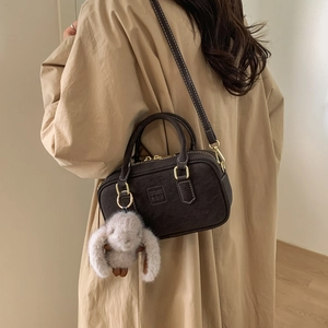 Detail of dark brown Boston bag with plush rabbit charm and embossed logo on trench coat
